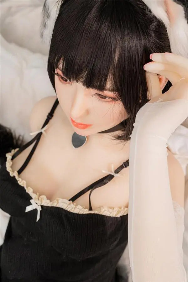 Amelie premium petite cosplay sex doll with short black bob in full black catgirl set with ears tail and collar, three-quarter seated view with soft natural lighting, best multi-height love doll by TopLoveDoll