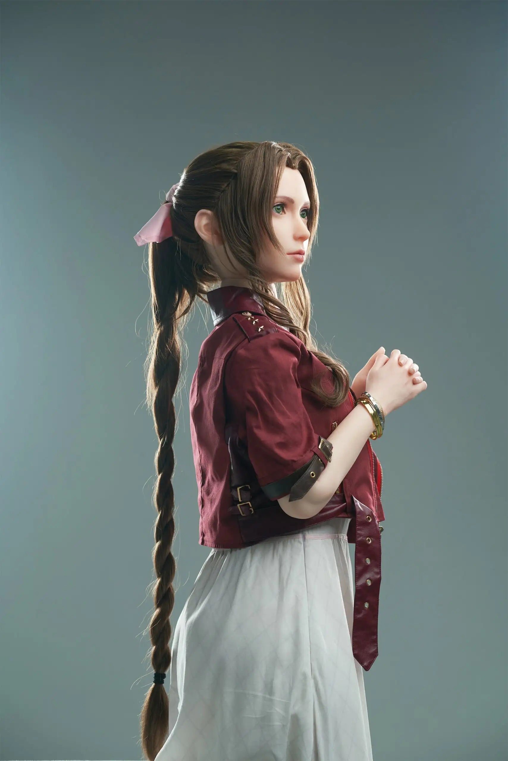 Seyo, brown wavy twin braids, pink hair bow, burgundy leather jacket, white deep-V slip dress, black leather mid-calf boots, green eyes, layered leather string choker, golden layered bracelet, looking at the camera like curious, grey studio background, standing, hands holding together like praying – Tifa Lockhart cosplay sex doll by TopLoveDoll