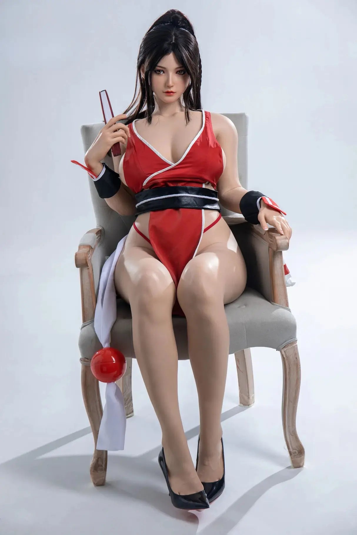 Aileen, long black hair, high ponytail with half-down hair, red Mai Shiranui signature kunoichi costume, holding her signature weapon(the fan), sex AF, sitting straight in a grey armchair and looking at the camera, full white studio background,  front view, gorgeous curves, full shot– cosplay sex doll by TopLoveDoll 