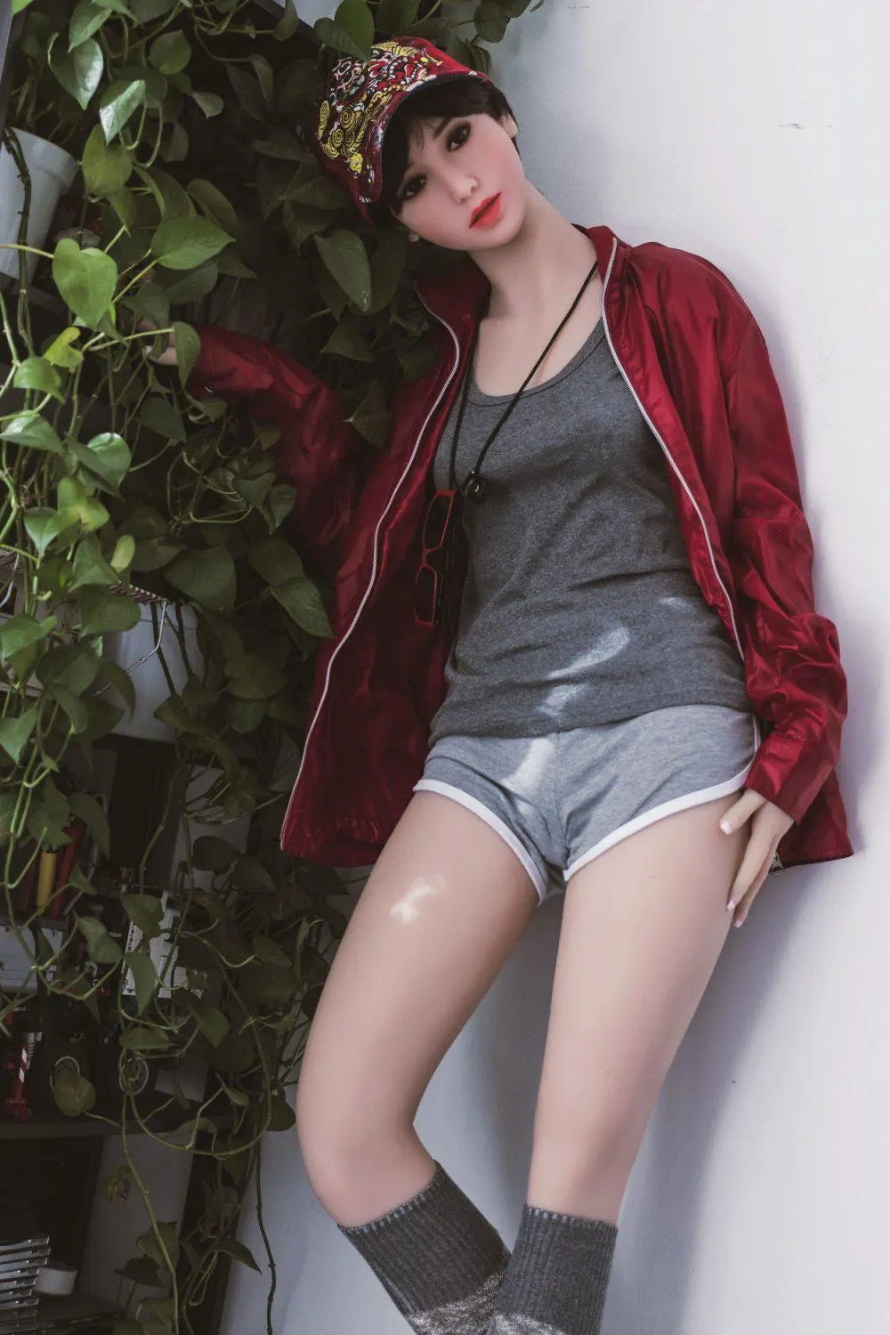 Amira short dark brown hair red lip grey tank denim shorts red jacket tomboy feminine contrast pose, standing next to the plants shelf  – girl-next-door companion sex doll by TopLoveDoll