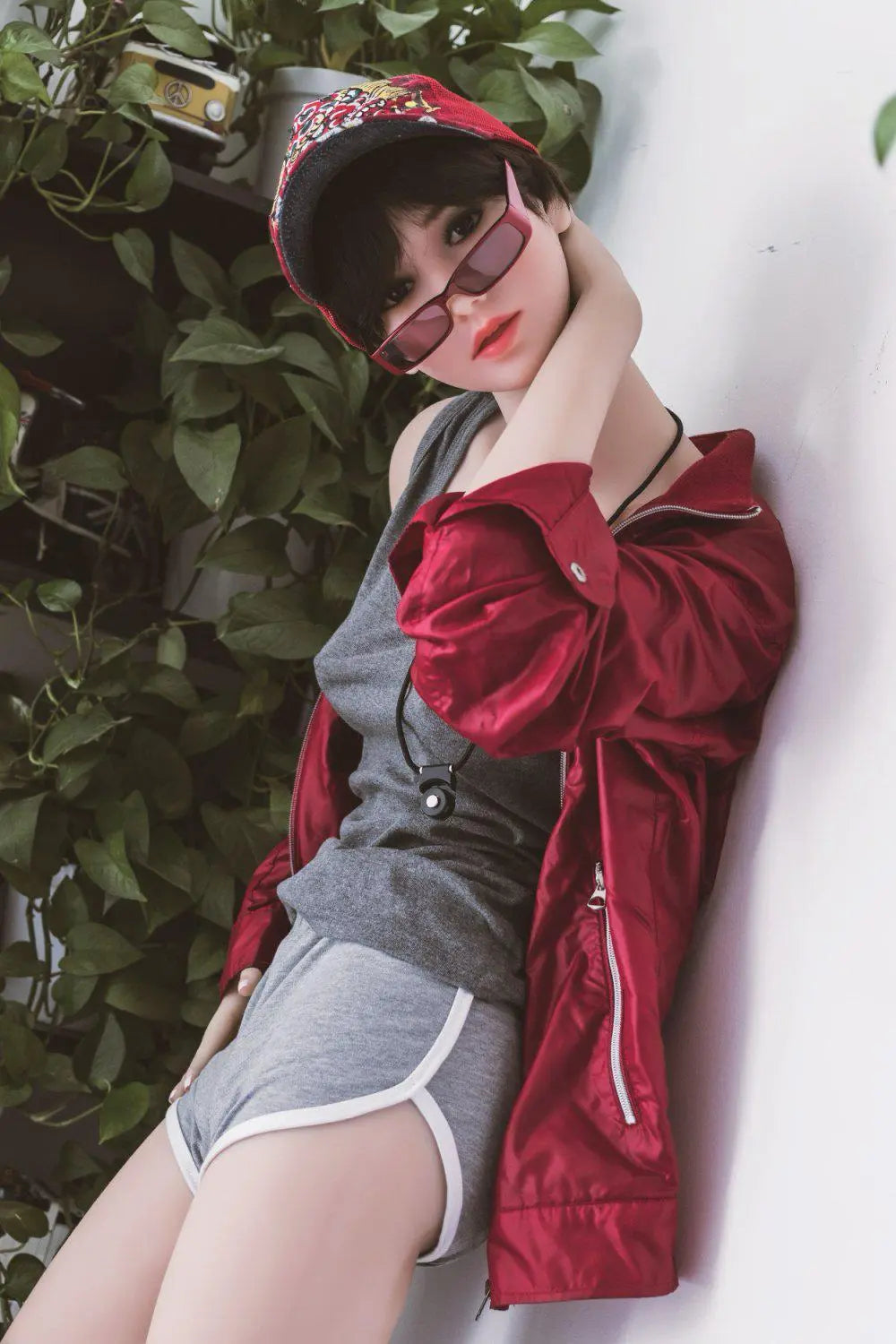 Amira short dark brown hair red lip grey tank denim shorts red jacket tomboy feminine contrast pose, standing next to the plants shelf, baseball hat, red sunglasses, side view– girl-next-door companion sex doll by TopLoveDoll