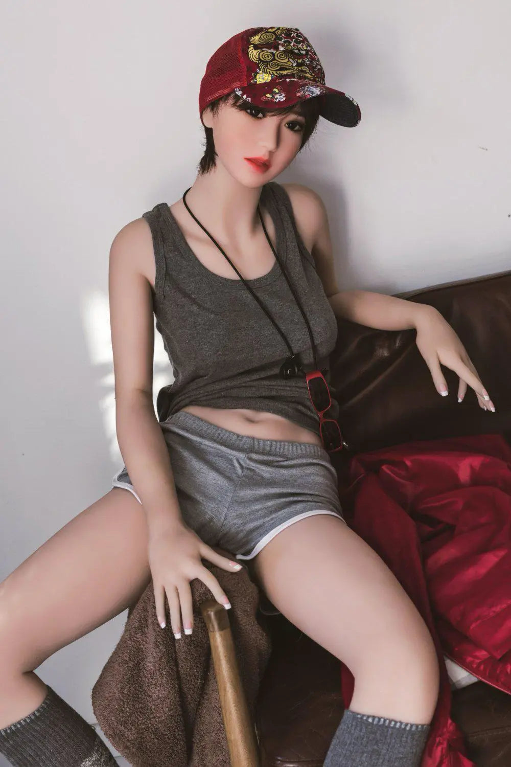 Amira short dark brown hair red lip grey tank denim shorts tomboy feminine, riding on the arm of the chair, baseball hat, red sunglasses on the neck lace,– girl-next-door companion sex doll by TopLoveDoll