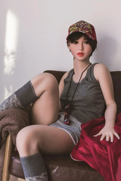 Amira short dark brown hair red lip grey tank denim shorts tomboy feminine, sitting in the armchair, baseball hat, red sunglasses on the neck lace, showing her tongue– girl-next-door companion sex doll by TopLoveDoll