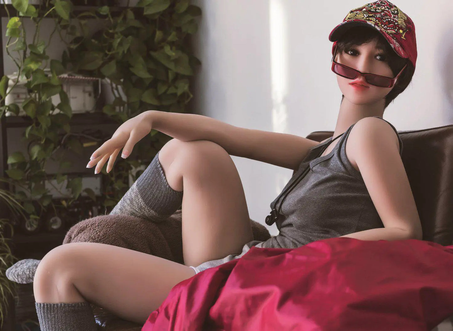 Amira short dark brown hair red lip grey tank denim shorts tomboy feminine, lying in the armchair, baseball hat, red sunglasses on the neck lace, horizontal profile– girl-next-door companion sex doll by TopLoveDoll