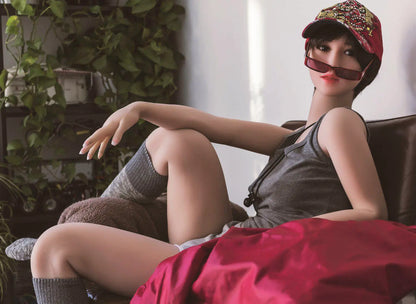 Amira short dark brown hair red lip grey tank denim shorts tomboy feminine, lying in the armchair, baseball hat, red sunglasses on the neck lace, horizontal profile– girl-next-door companion sex doll by TopLoveDoll