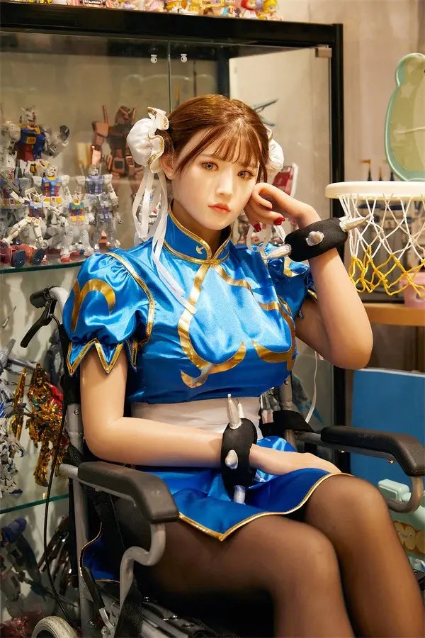 Araya Street Fighter Chun-Li cosplay sex doll, sitting in front of her home figurine exhibits, grey contacts, spiky bracelets- blue qipao, high twin buns - Asian beauty elevated by TopLoveDoll