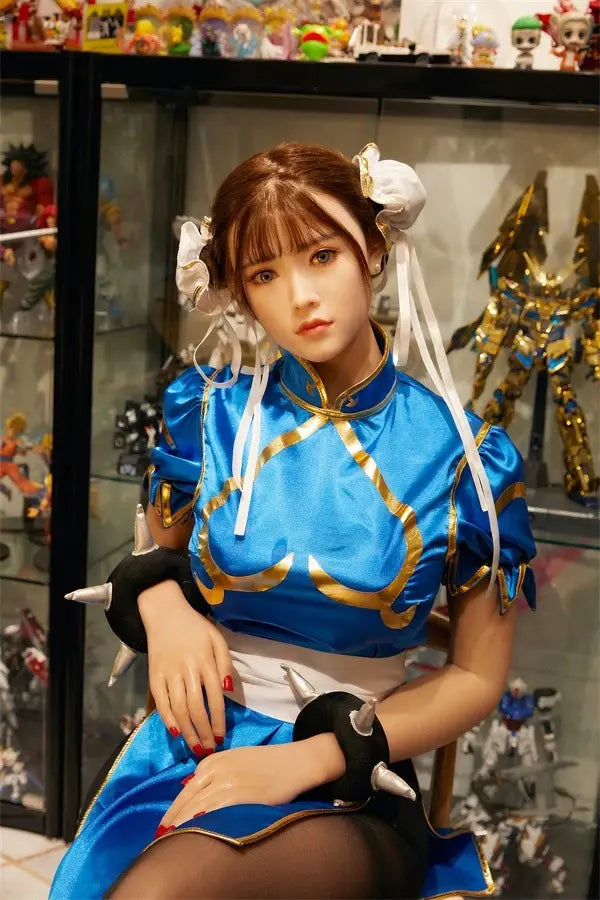 Araya Street Fighter Chun-Li cosplay sex doll, sitting in front of her home figurine exhibits, grey contacts, spiky bracelets, red nails- blue qipao, high twin buns - Asian beauty elevated by TopLoveDoll