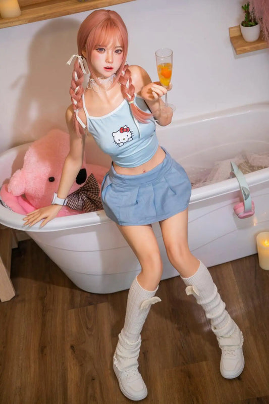 Amor sex doll full-body leaning against white bathtub in cozy pink bathroom setting, long salmon pink hair styled in twin braids with white ribbon bow hair ties, soft brown eyes with innocent direct gaze and parted nude lips, delicate silver chain necklace, silver watch on wrist, light blue Hello Kitty graphic spaghetti-strap crop top with bare midriff, light blue pleated mini skirt, white knee-high platform sneaker boots, one hand raised holding glass of orange juice, other hand resting on bathtub edge, la